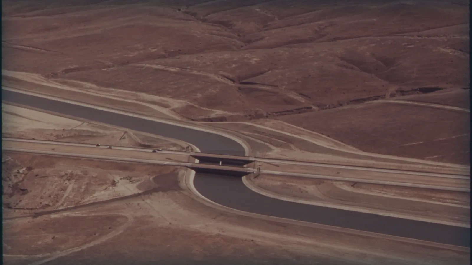 Canal de riego cruzando tierras de cultivo áridas, vista aérea.